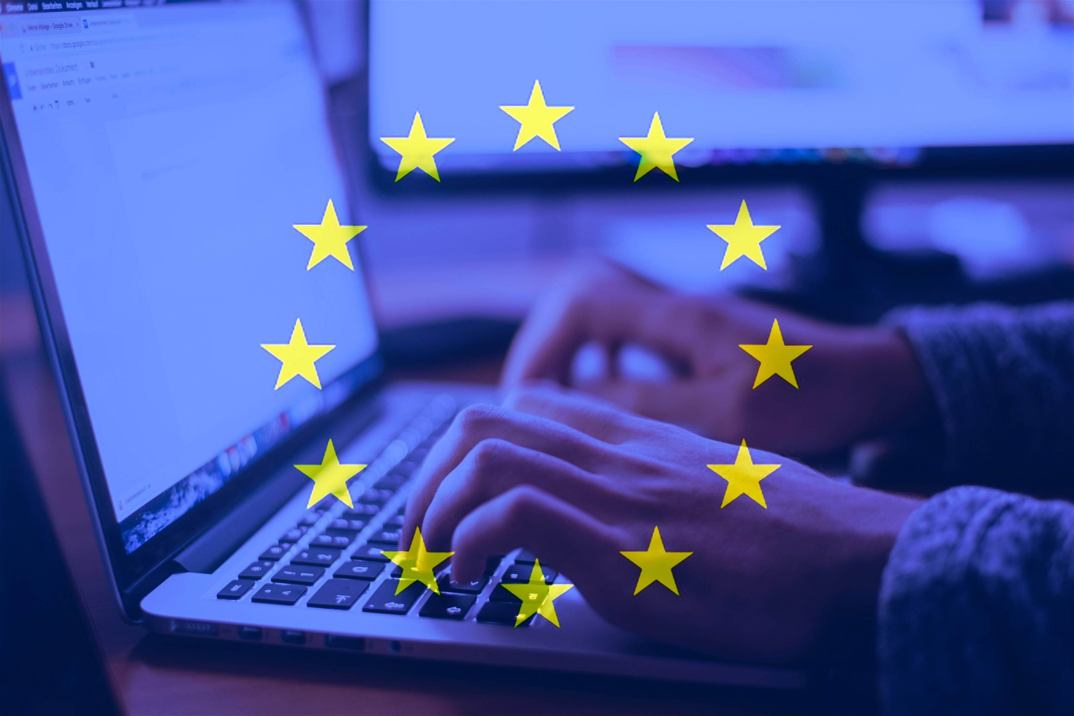 Hands typing on a laptop beneath a circle of yellow EU stars