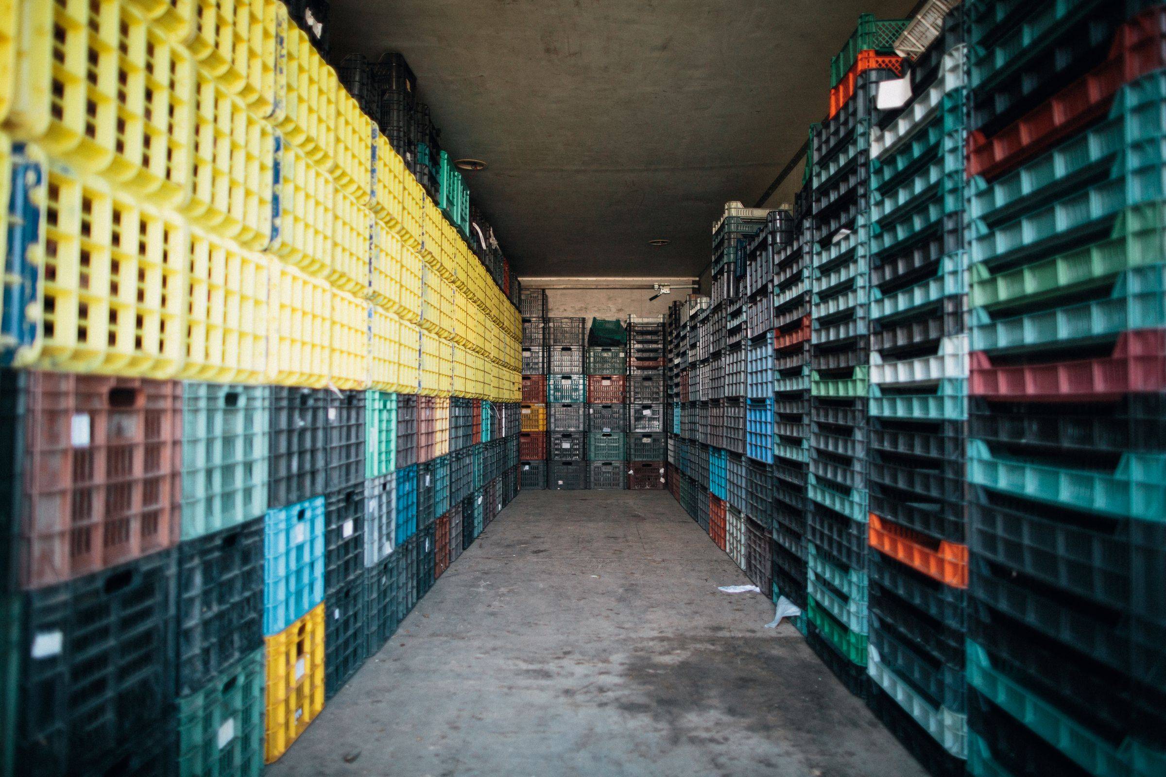 A corridor between tall stacks of plastic crates in a storehouse