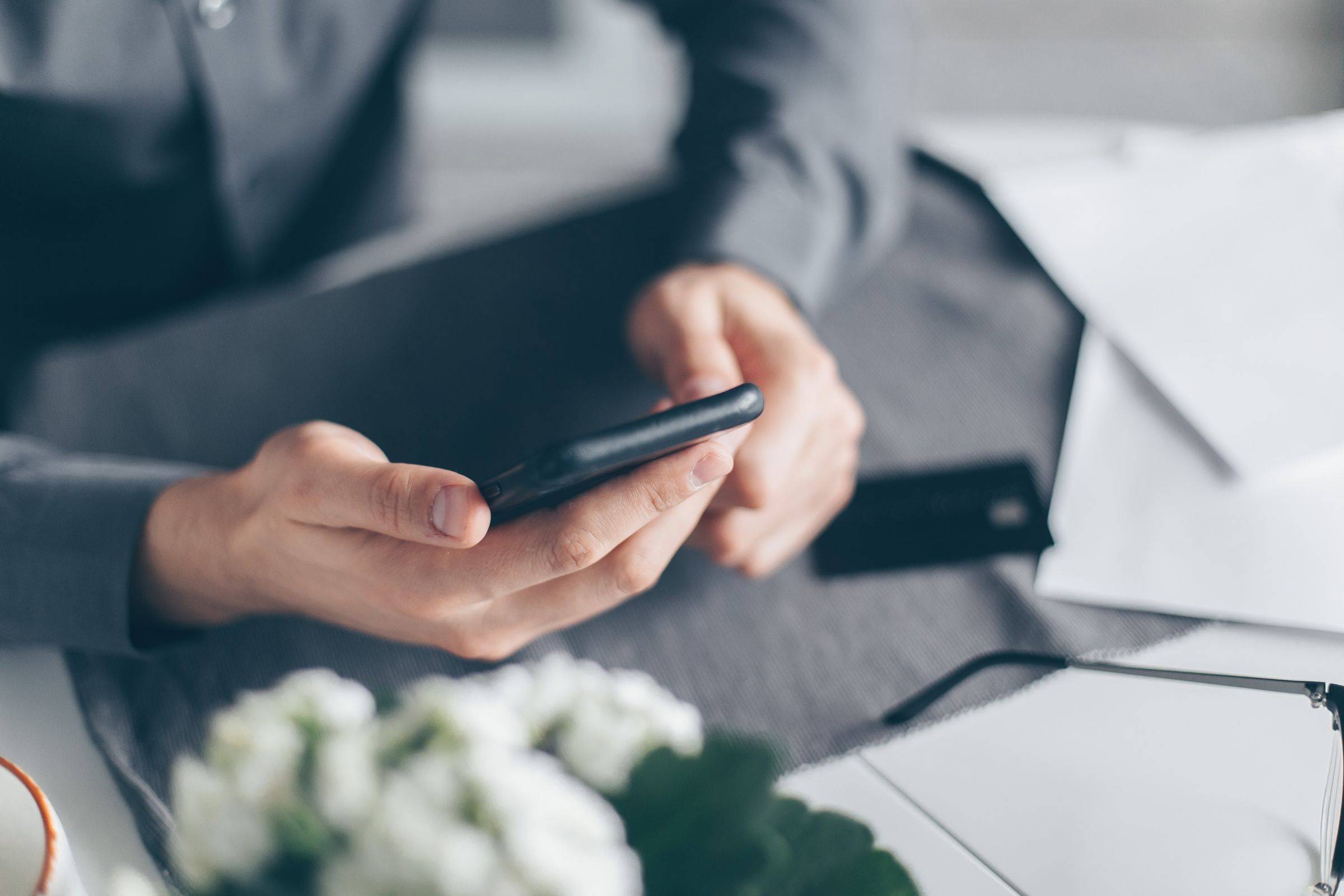 Ruka drží telefon nad stolem s fakturami