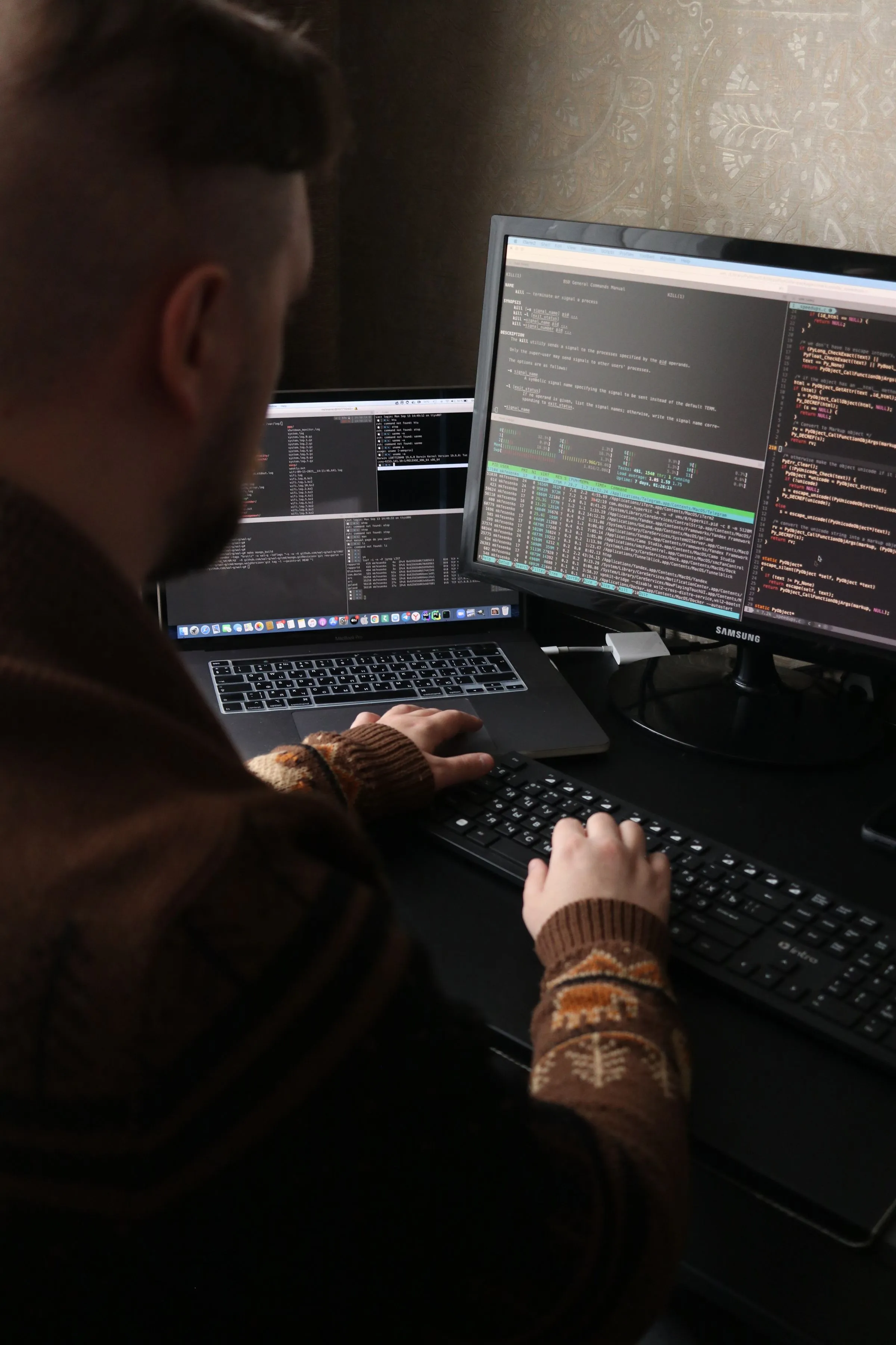 A developer at two dark monitors full of code, seen from behind