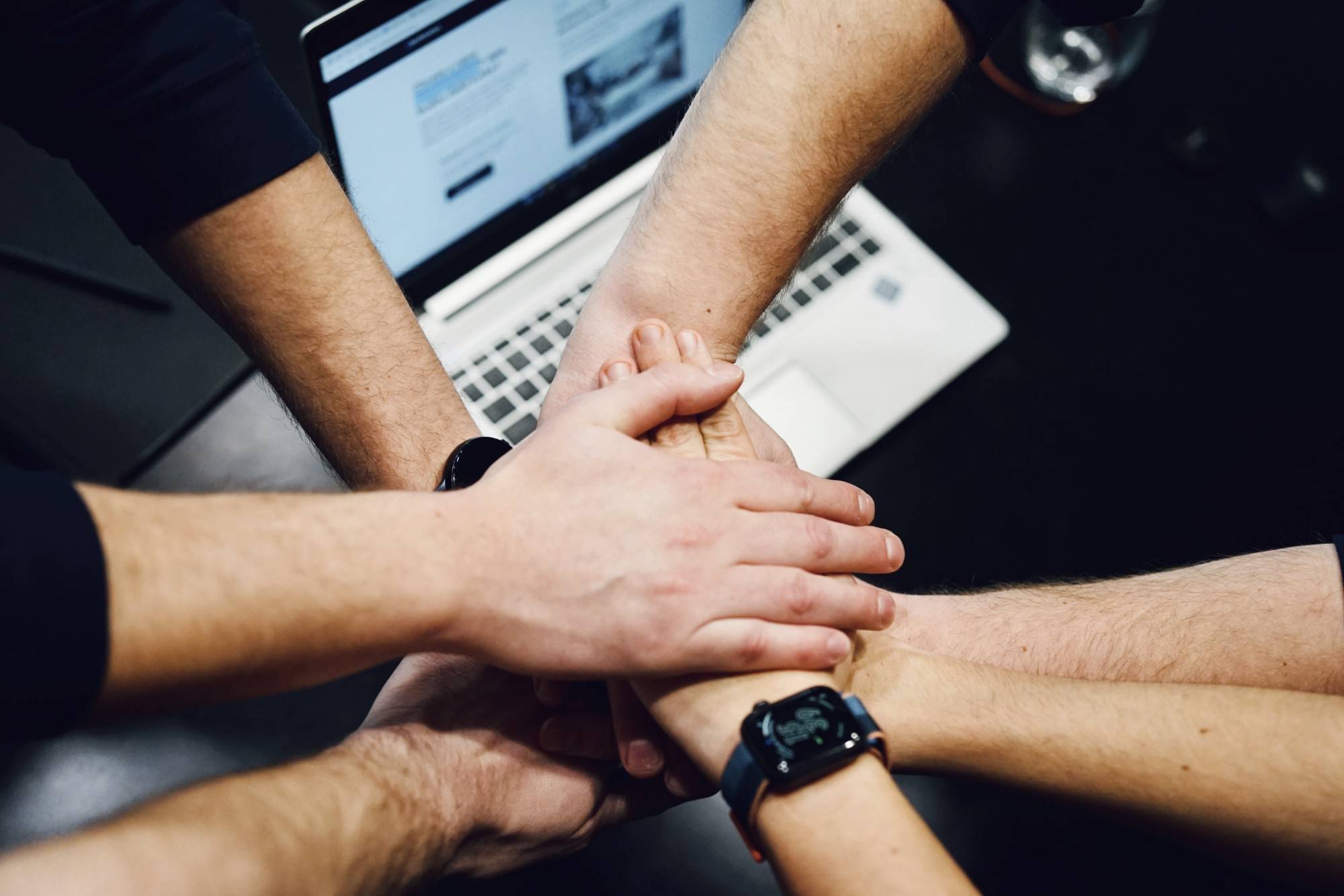 Hands of the Techmates team stacked together over a laptop