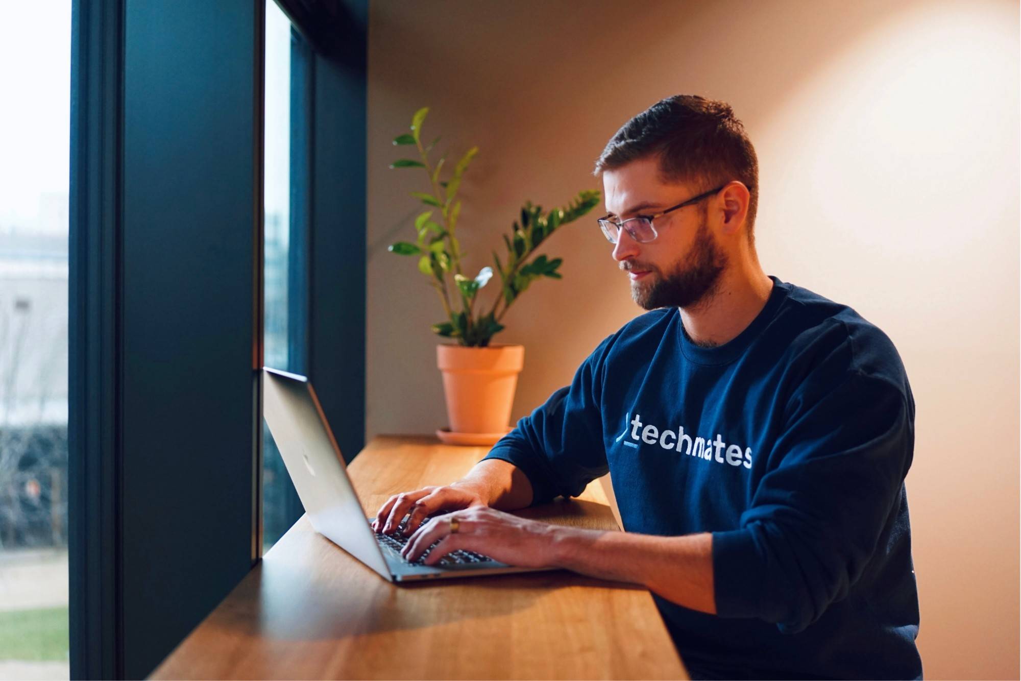 Člen týmu Techmates pracuje na notebooku u okna